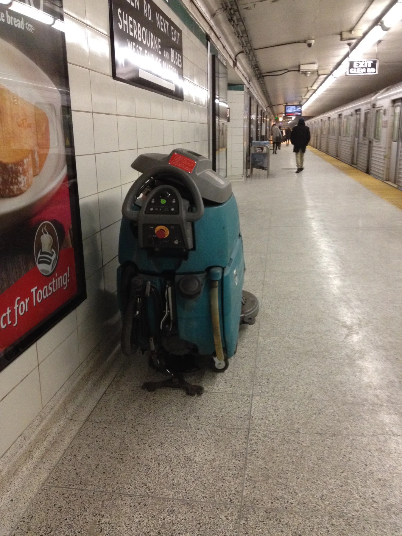 A walk-behind floor scrubber parked on a tiled subway platform.